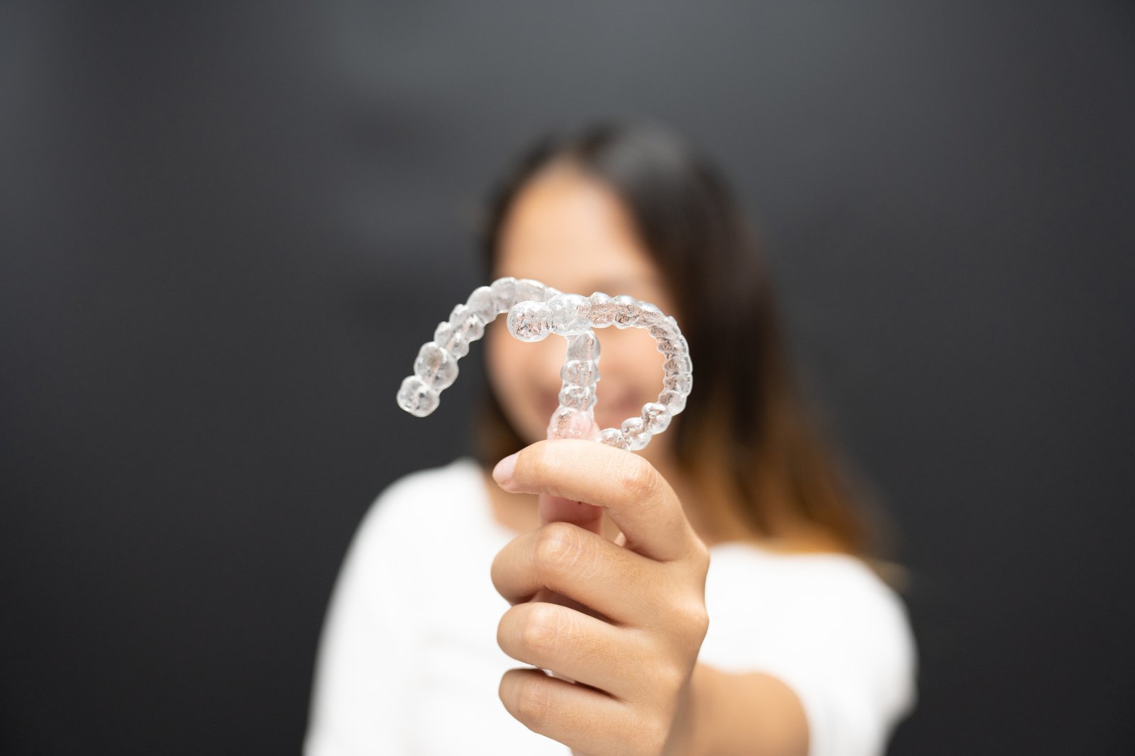 Women hand hold inivisalign braces, transparent aligner, invisible retainer or orthodontic silicone trainer with blur mile in background. A way to have a beautiful smile.
