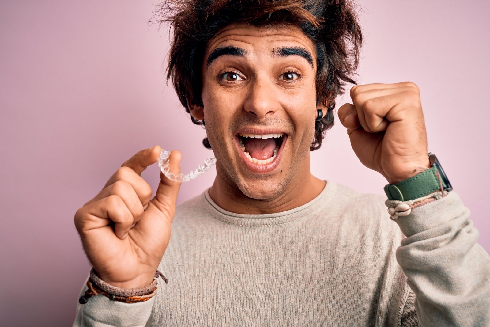 Young handsome man holding aligner standing over isolated pink background screaming proud and celebrating victory and success very excited, cheering emotion