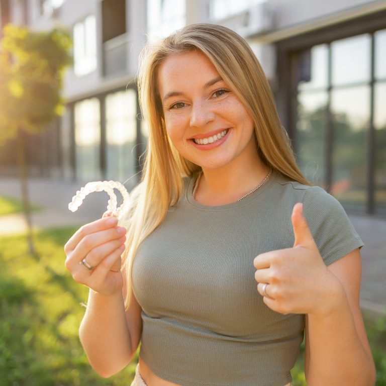 Smiling Woman Holding Clear Aligners Outdoors Giving a Thumbs Up